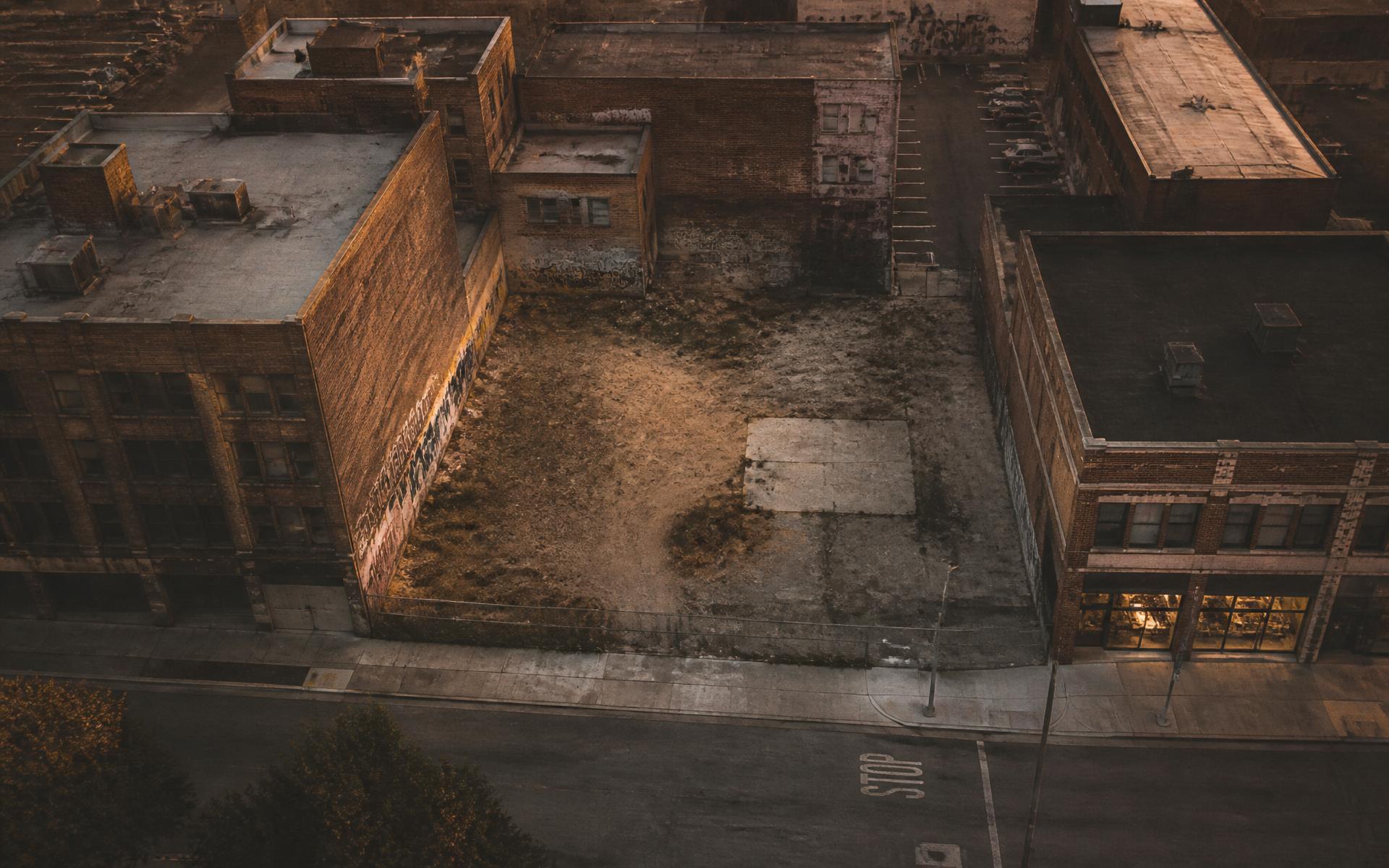 An empty urban corner lot at golden hour, surrounded by old brick warehouses.